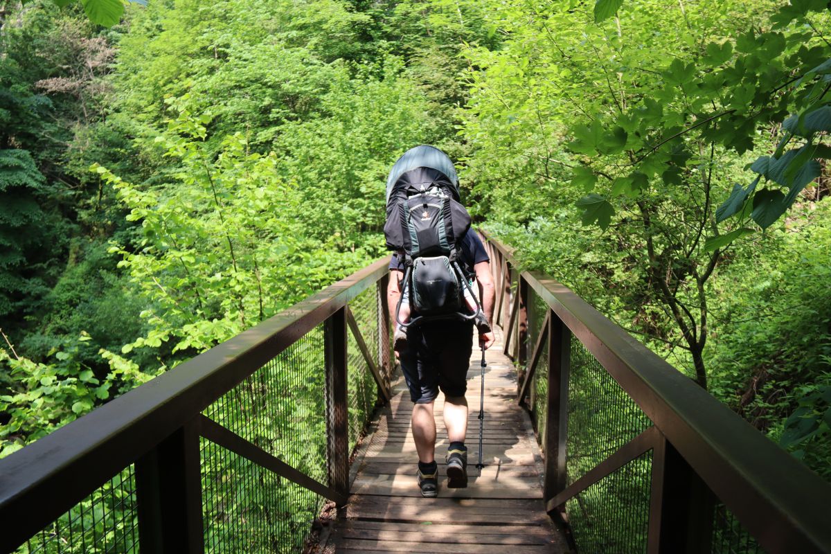 Papa mit Deuter Kindertrage auf Brücke in einem Wald der Areuse Schlucht